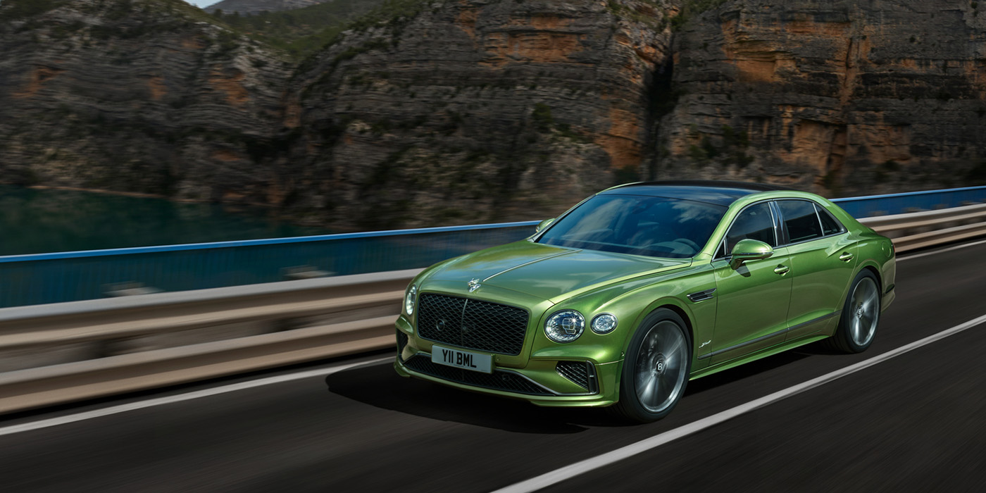 Emil Frey Exclusive Cars GmbH | Bentley München Bentley New Flying Spur Speed v8 hybrid sedan driving dynamically on a mountain road in Tourmaline Green paint