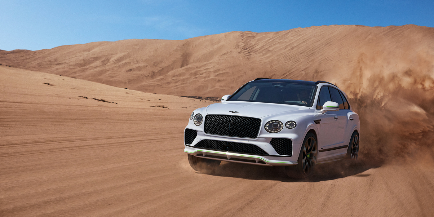 Emil Frey Exclusive Cars GmbH | Bentley München Bentley Bentayga Speed SUV front three quarter in Snow Quarts Pearlescent by Mulliner white paint driving dynamically through the desert