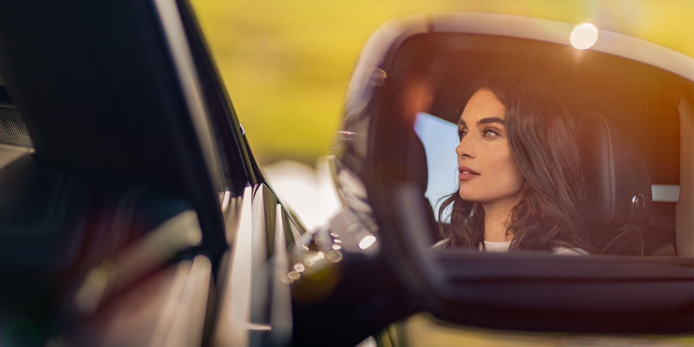 Emil Frey Exclusive Cars GmbH | Bentley München profile of dark haired woman's face in mirror of Bentley car in sunlight