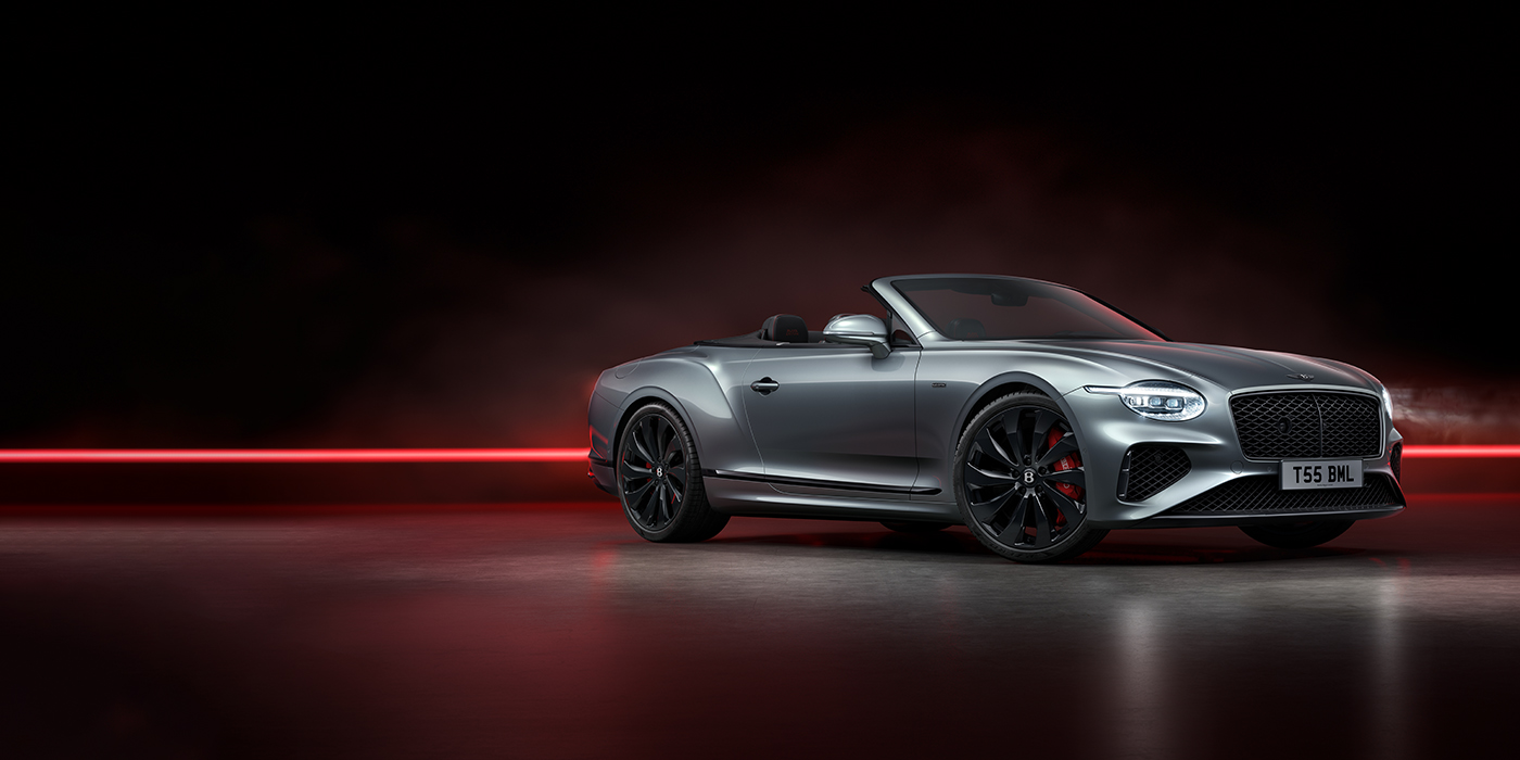 Emil Frey Exclusive Cars GmbH | Bentley München Bentley Continental GTC Black Edition convertible front three quarters in Hallmark silver against a dark grey and red background