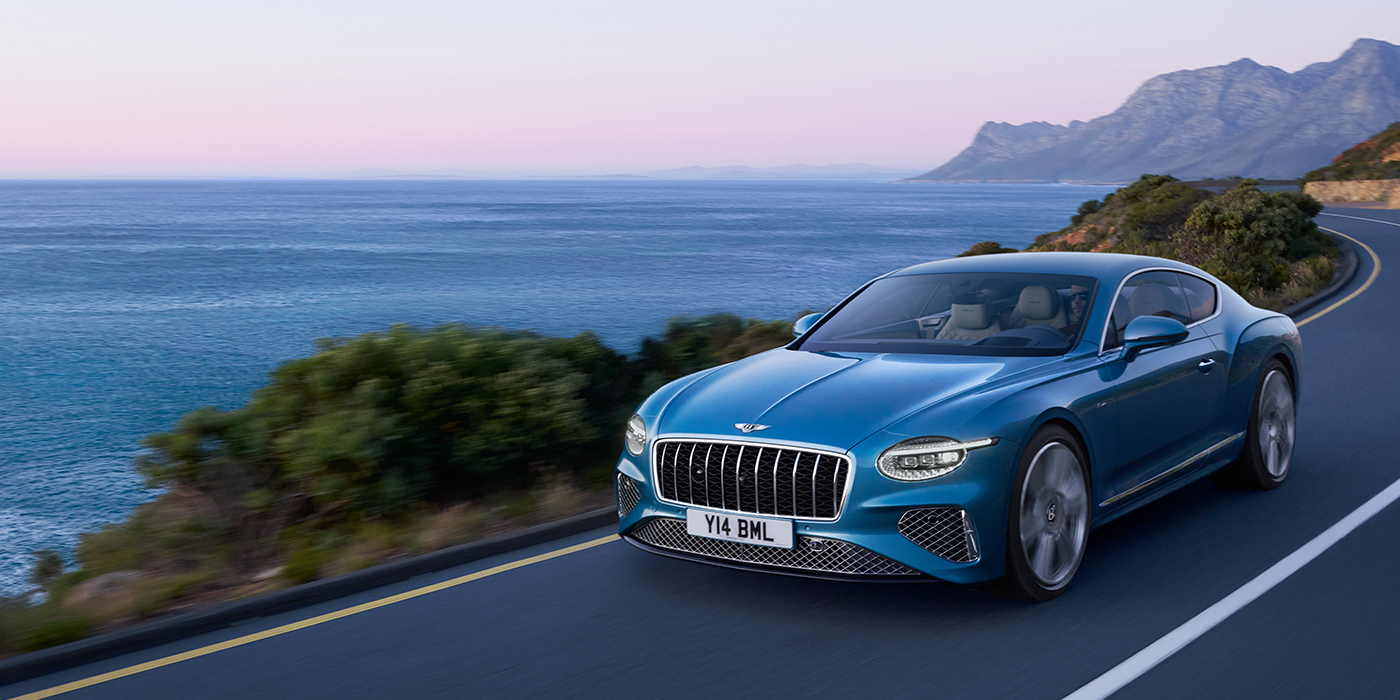 Emil Frey Exclusive Cars GmbH | Bentley München New Bentley Continental GT Azure coupe in Light Windsor blue paint with 22 inch Azure wheels and chrome grill, driving dynamically by the sea