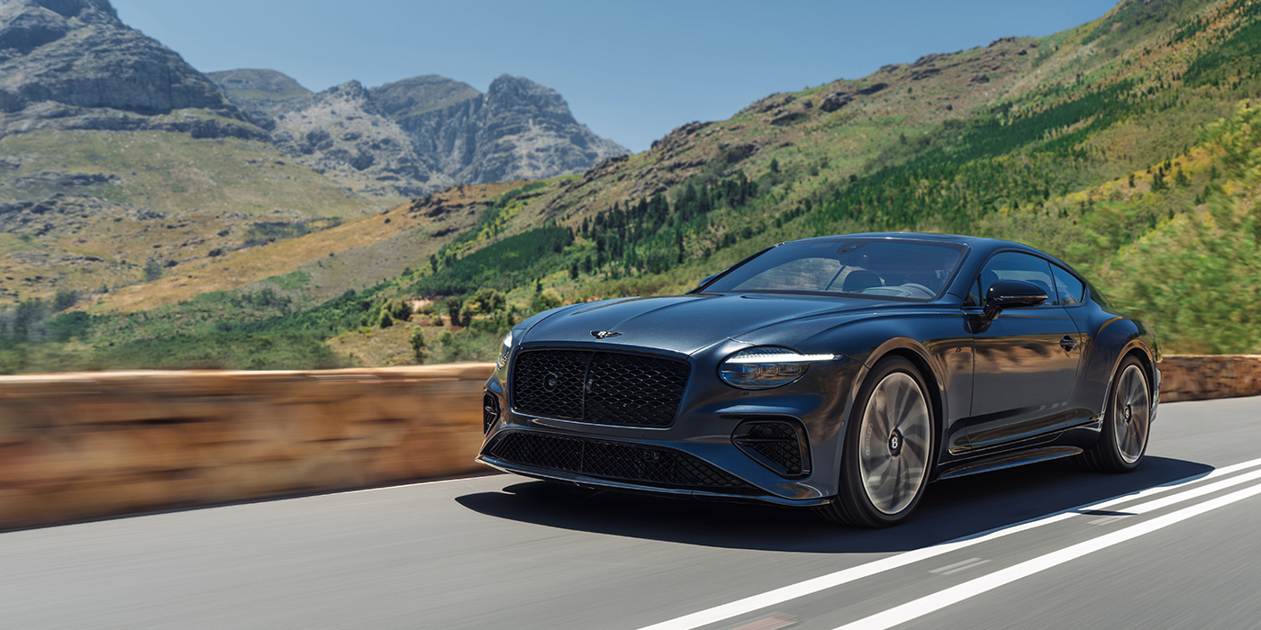 Emil Frey Exclusive Cars GmbH | Bentley München Bentley Continental GT coupe in Thunder paint and 22" ten swept spoke wheels front 3/4 driving on mountain road