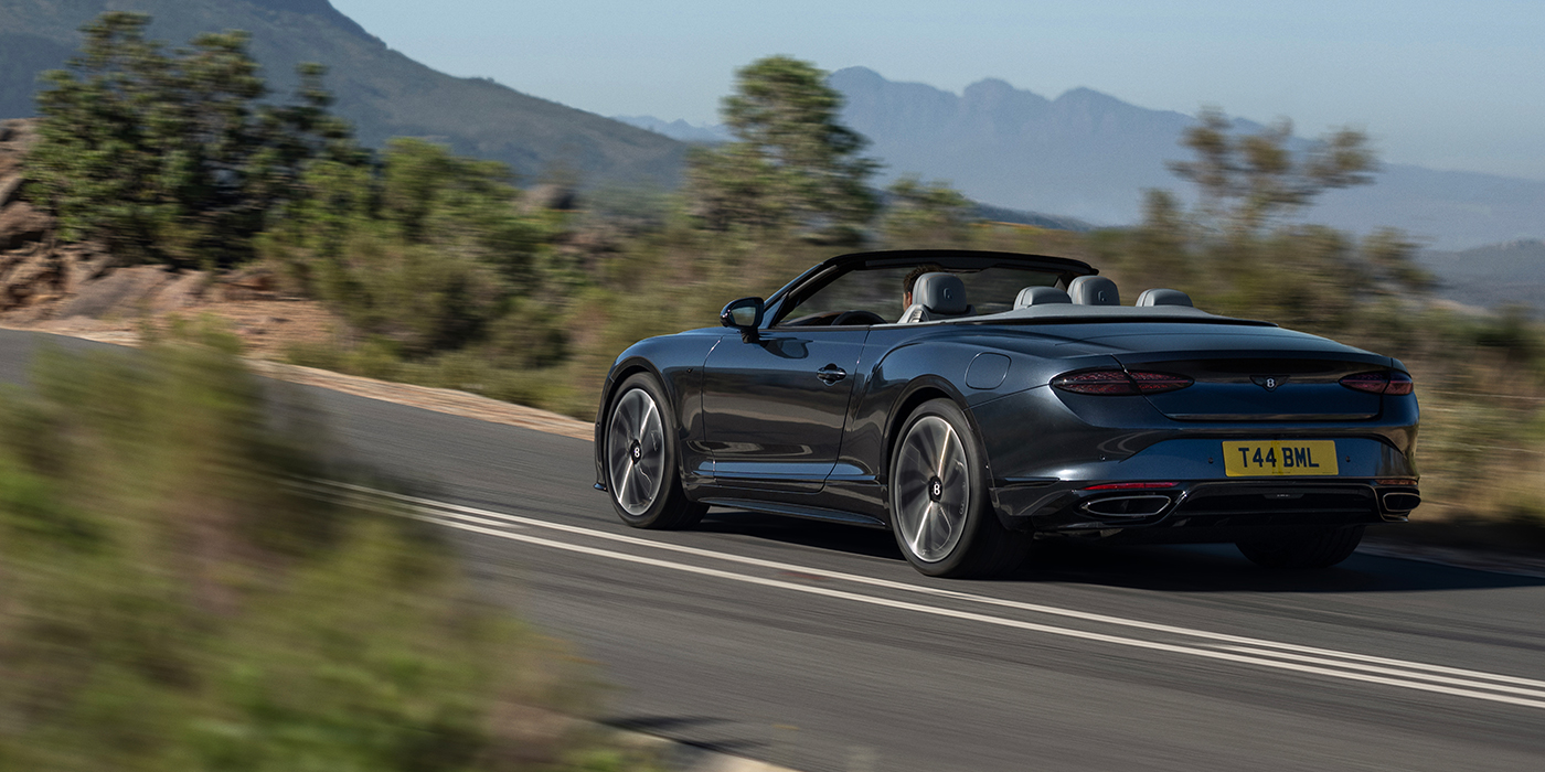 Emil Frey Exclusive Cars GmbH | Bentley München Bentley Continental GTC S convertible in Thunder blue paint rear 3/4 driving on mountain road