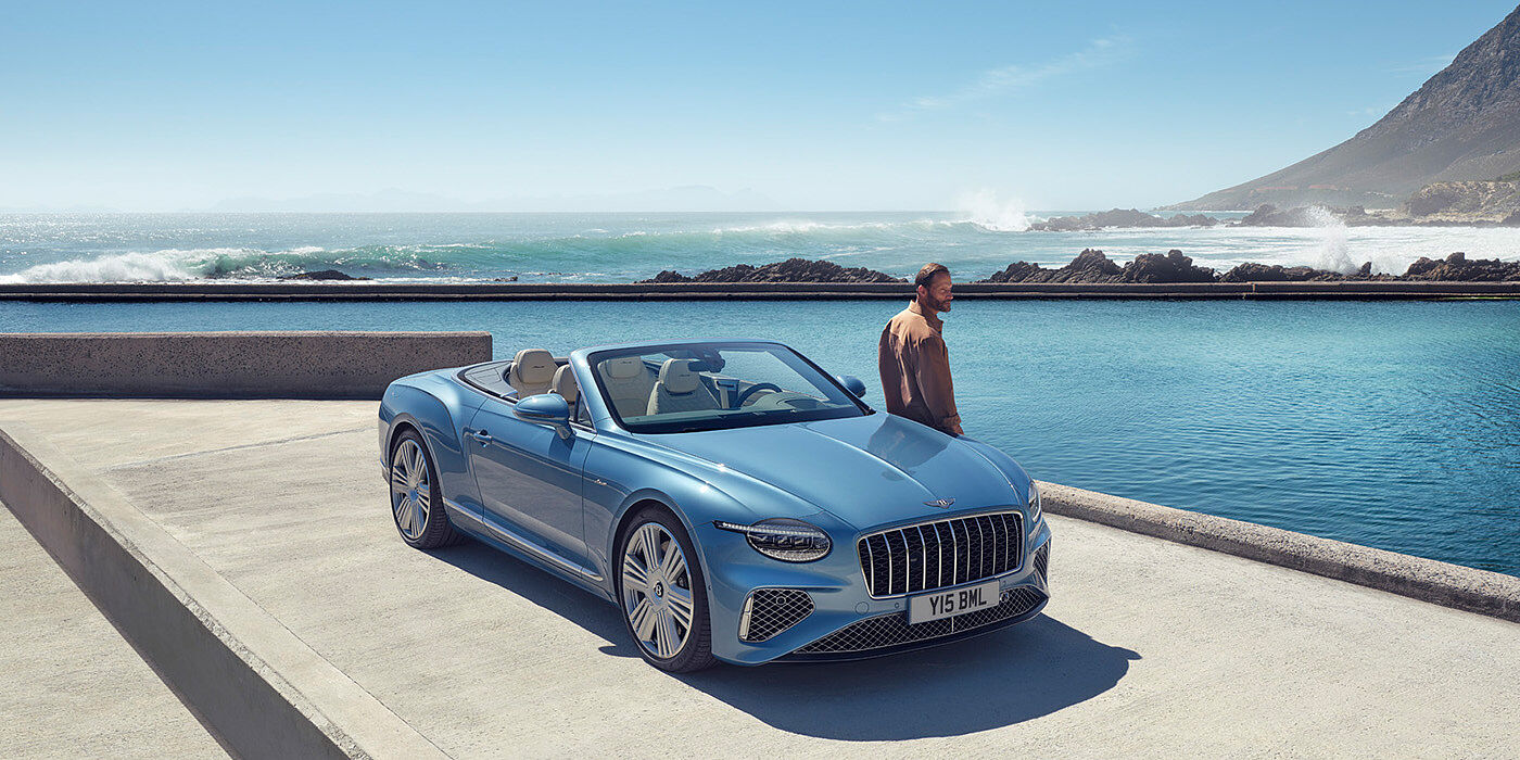 Emil Frey Exclusive Cars GmbH | Bentley München New Bentley Continental GTC Azure convertible front view in Light Windsor blue paint with 22 inch ten spoke wheels parked by the sea in the sunshine