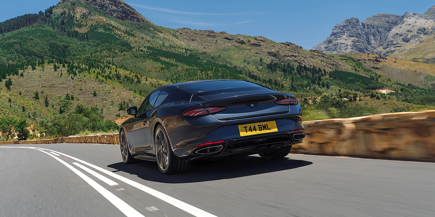 Emil Frey Exclusive Cars GmbH | Bentley München Bentley Continental GT coupe in Thunder paint rear driving through mountains in sunshine