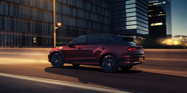 Emil Frey Exclusive Cars GmbH | Bentley München Bentley Bentayga Extended Wheelbase Mulliner SUV in Cricket Ball red paint driving dynamically in city at night